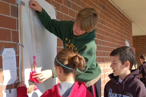 students measuring doll and string with ruler taped to wall